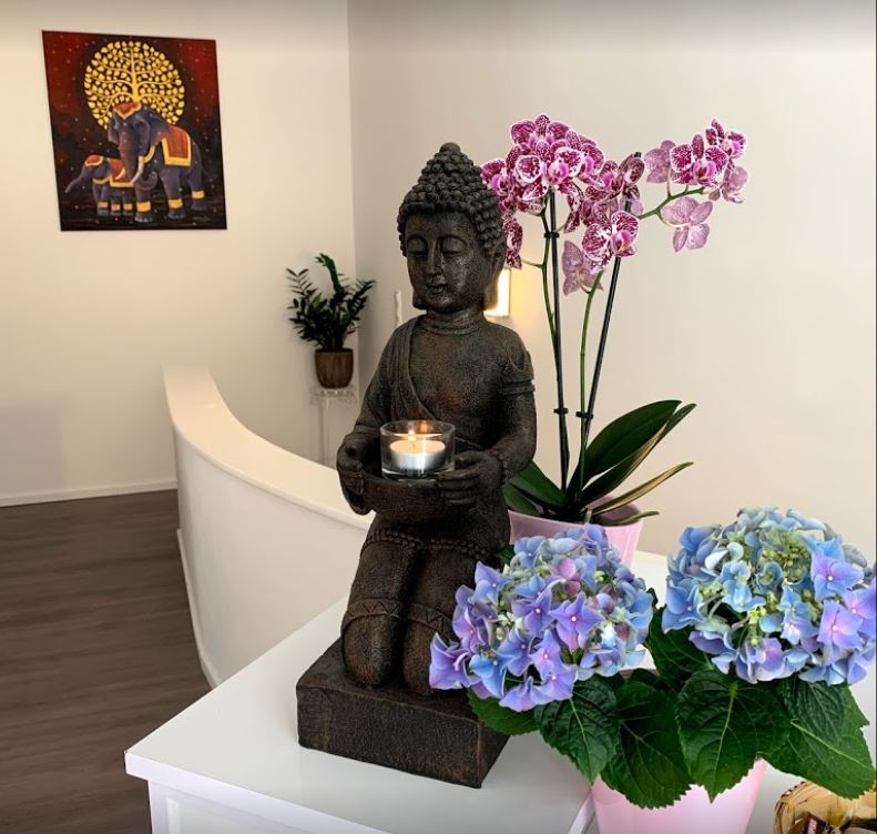 Thailändische Statue mit Kerze und Blumen